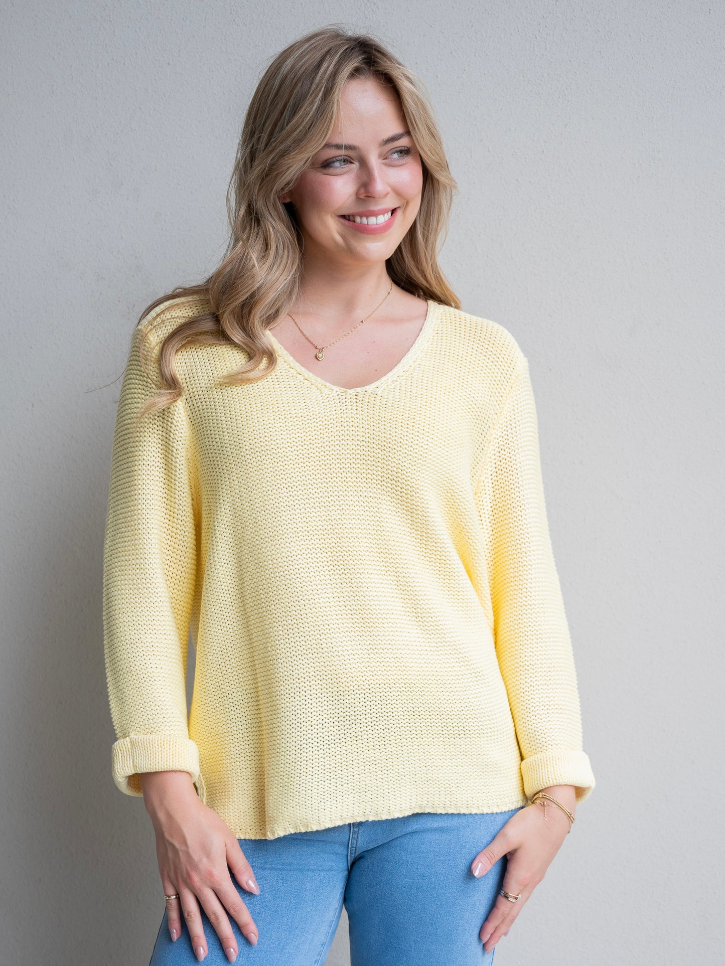 Woman wearing a yellow sweater and blue jeans against a plain background