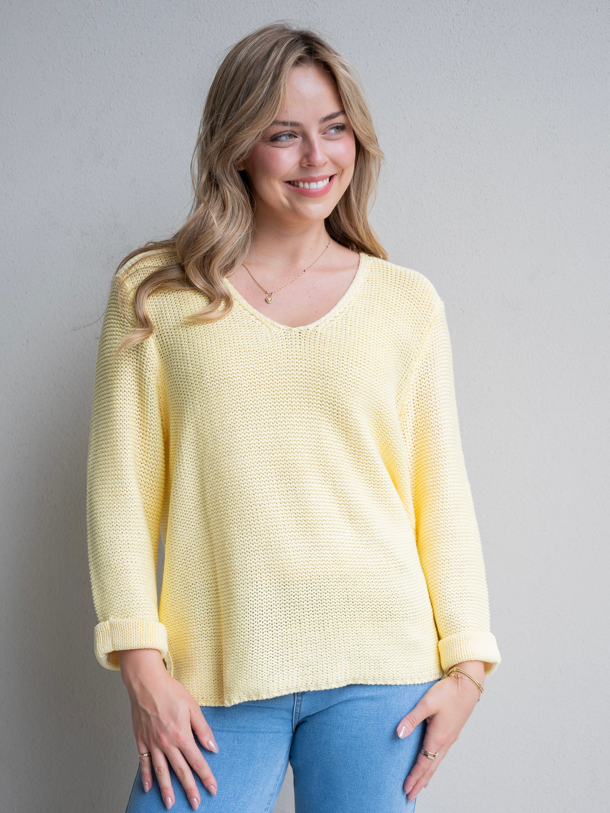 Woman wearing a yellow sweater and blue jeans against a plain background